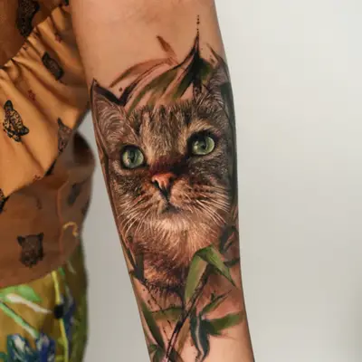 Realistic cat tattoo on forearm with foliage.
