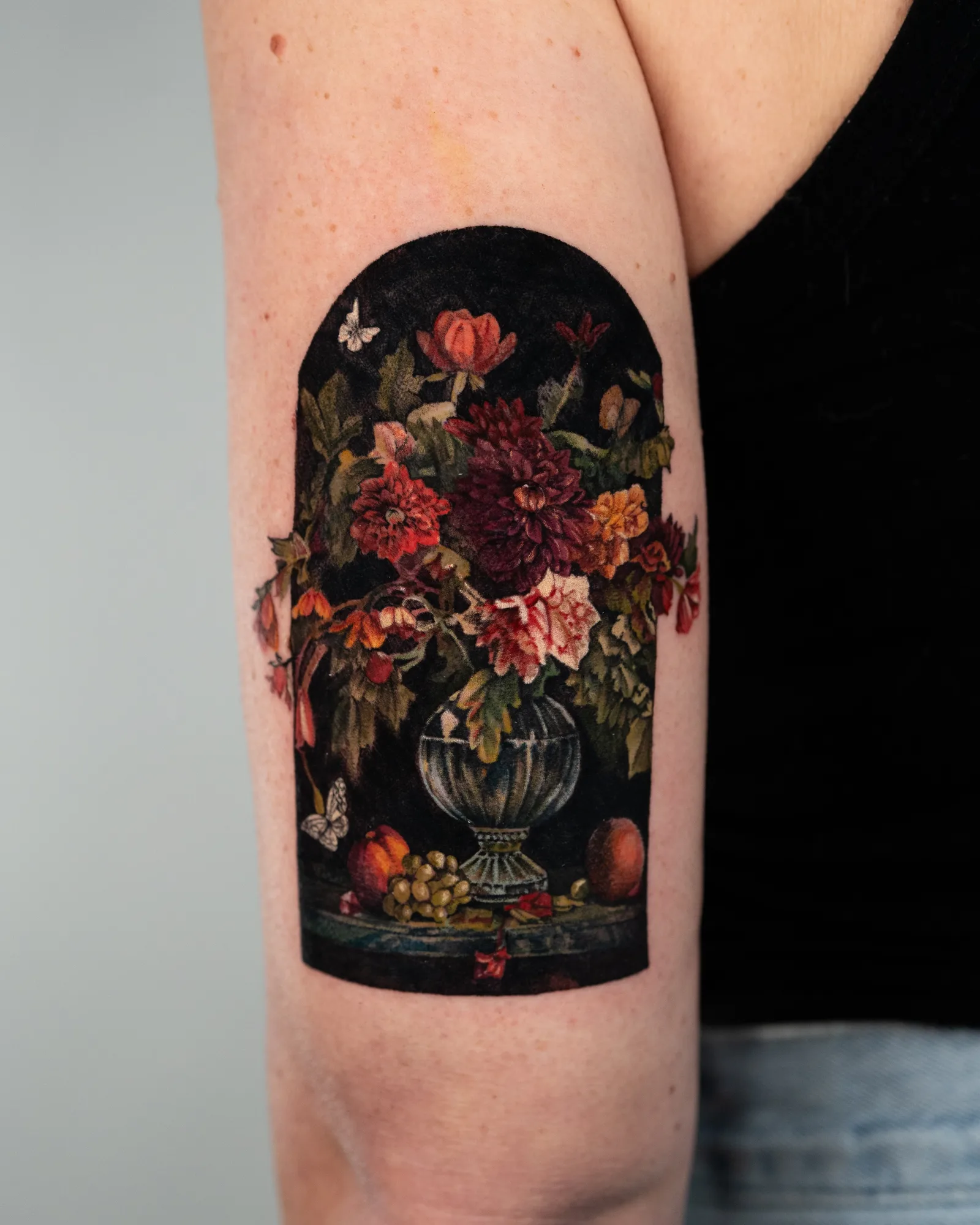 Tattoo of a floral arrangement in a vase on upper arm.