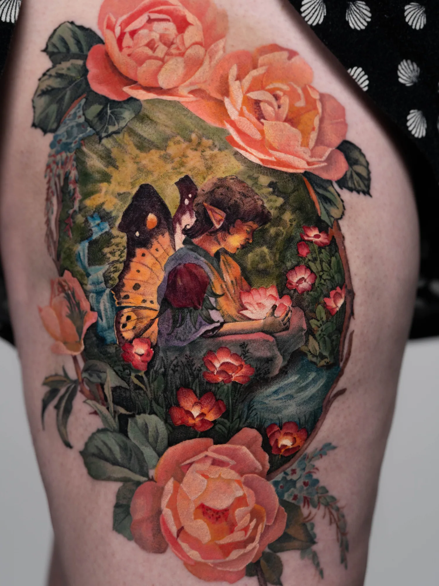 A colorful tattoo of a fairy with butterfly wings surrounded by flowers on the thigh.