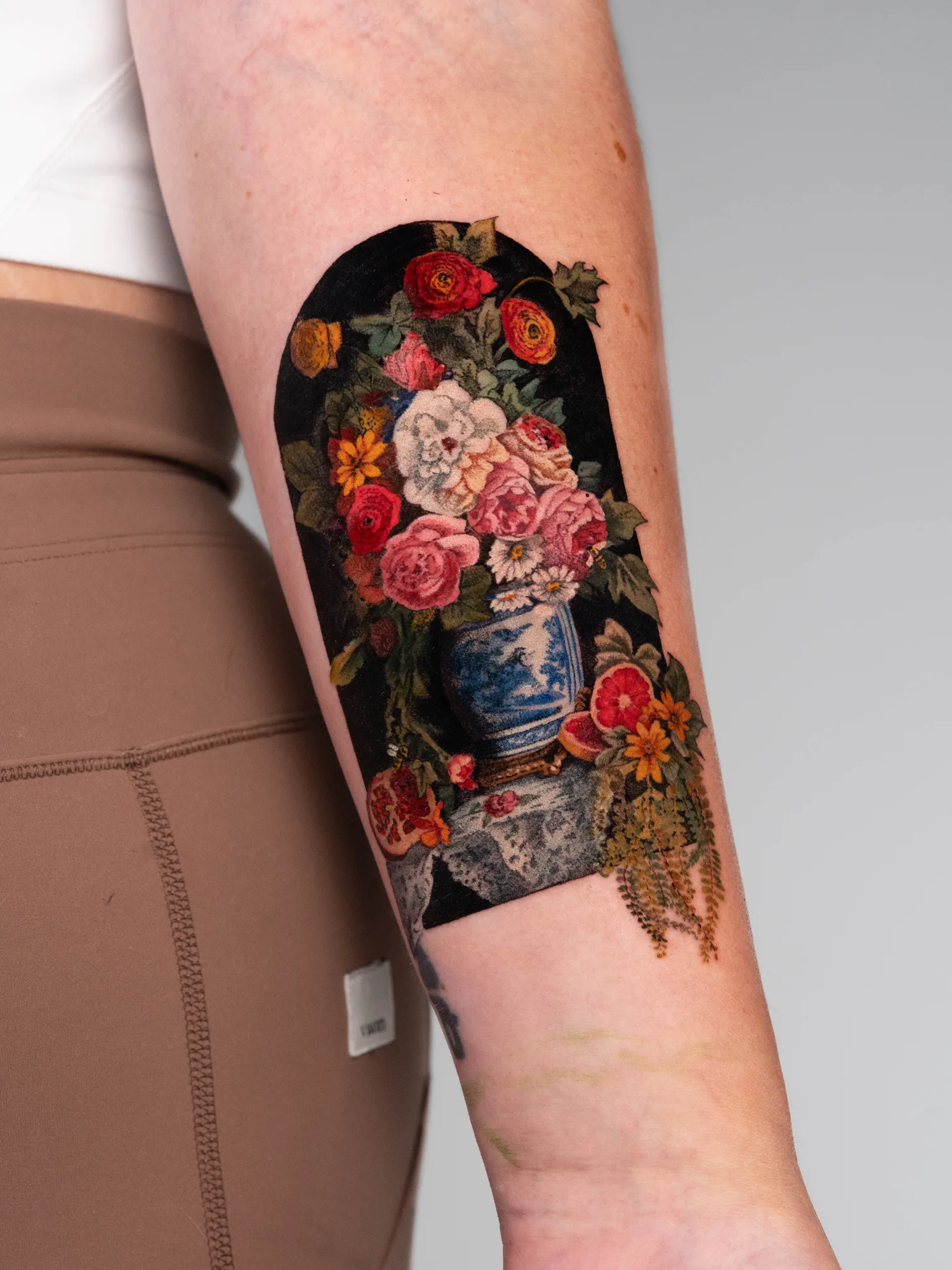 A colorful floral tattoo of a Dutch floral painting on the inner forearm featuring a vase and intricate flowers.