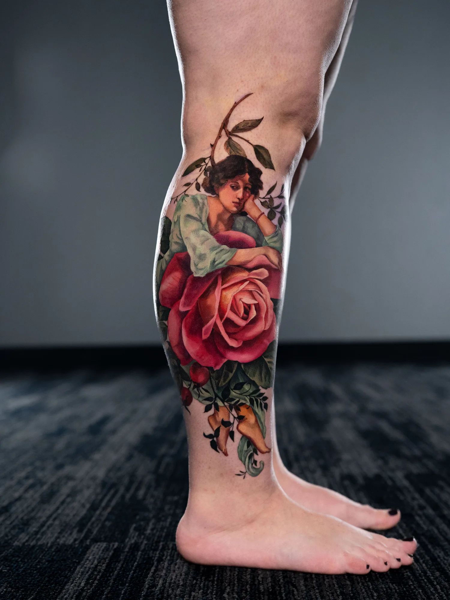 Tattoo of a lady resting on a flower on the lower leg in a painterly style.