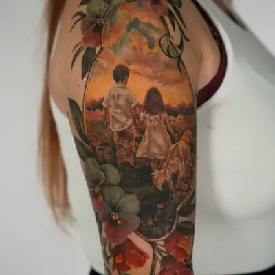 Landscape tattoo of a boy and a girl with a dog in a field during a sunset in a gold frame with flowers