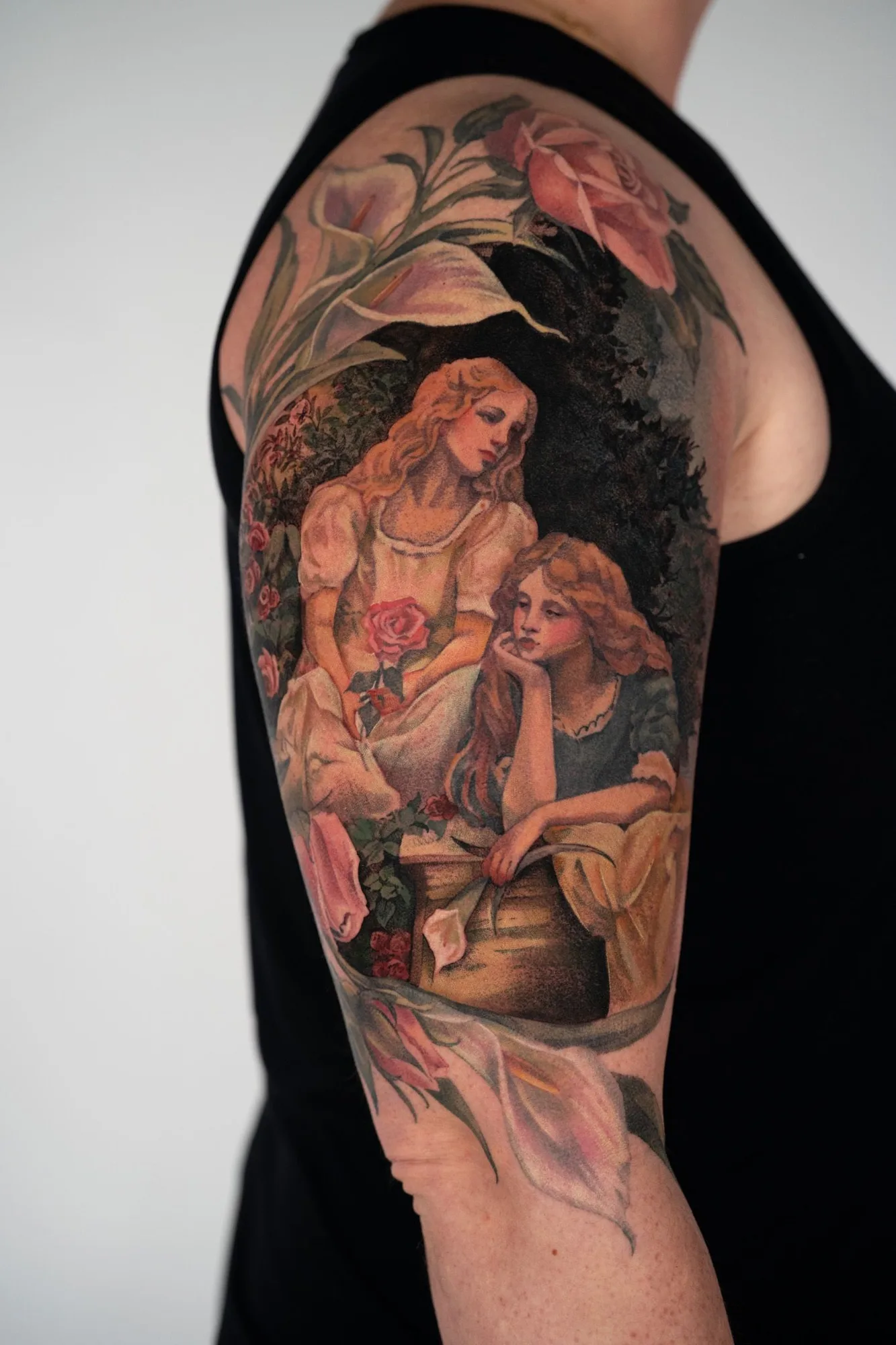 Painterly tattoo of two girls framed by rose and lily flowers.