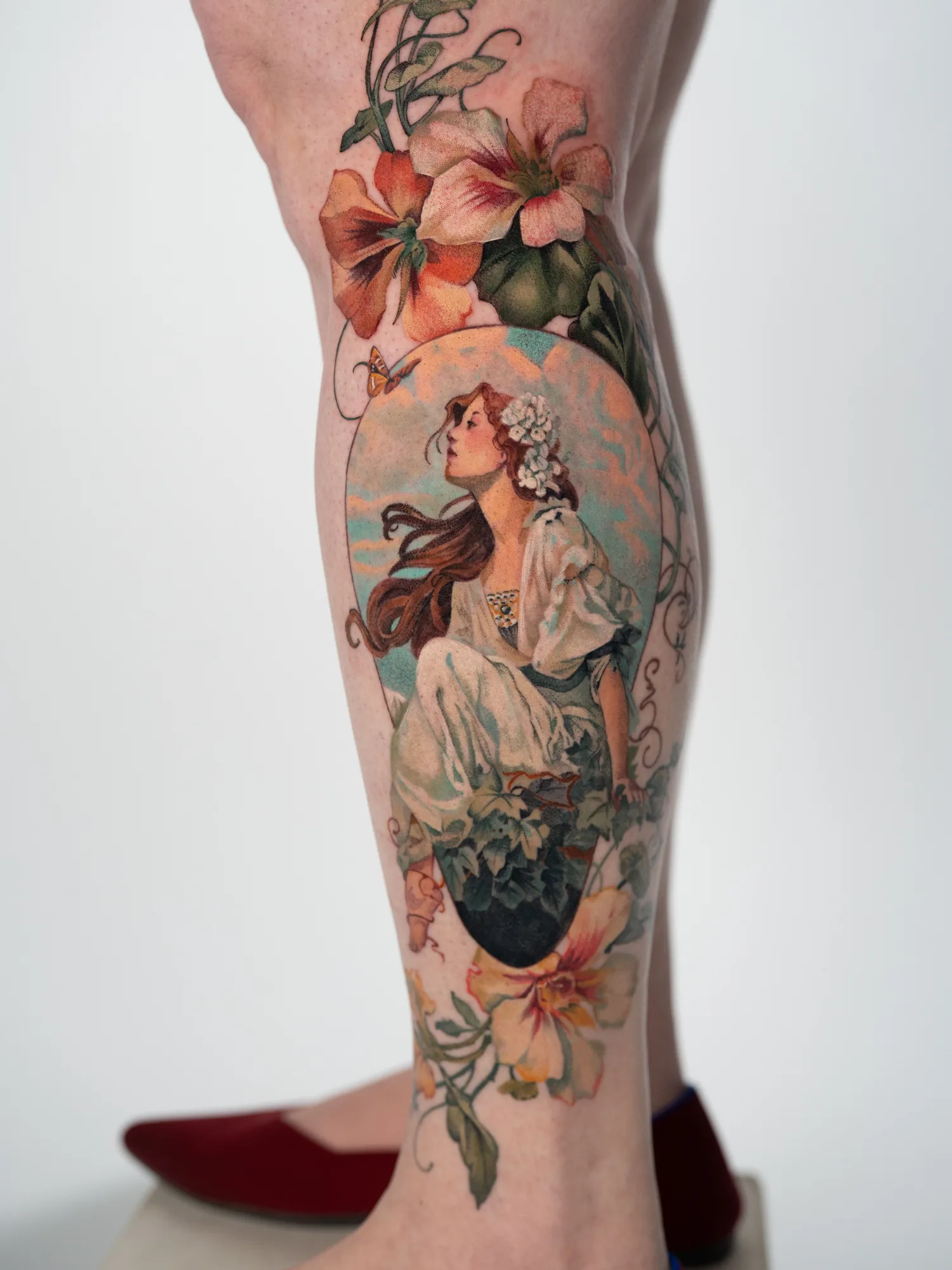 Colorful tattoo of a woman with flowers on a leg in a painterly frame.