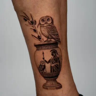 Tattoo of a vase with greek patterns and designs and an owl with an olive branch perched at the top.