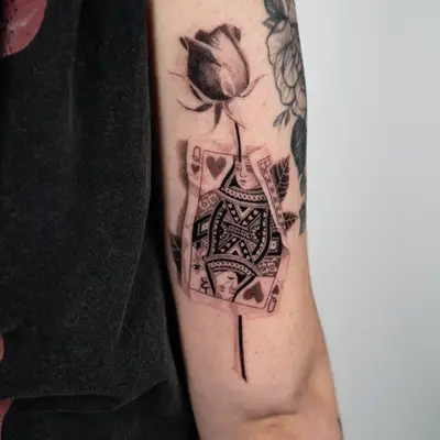 Micorealism tattoo of a crumpled Queen of Hearts with a rose going through it.