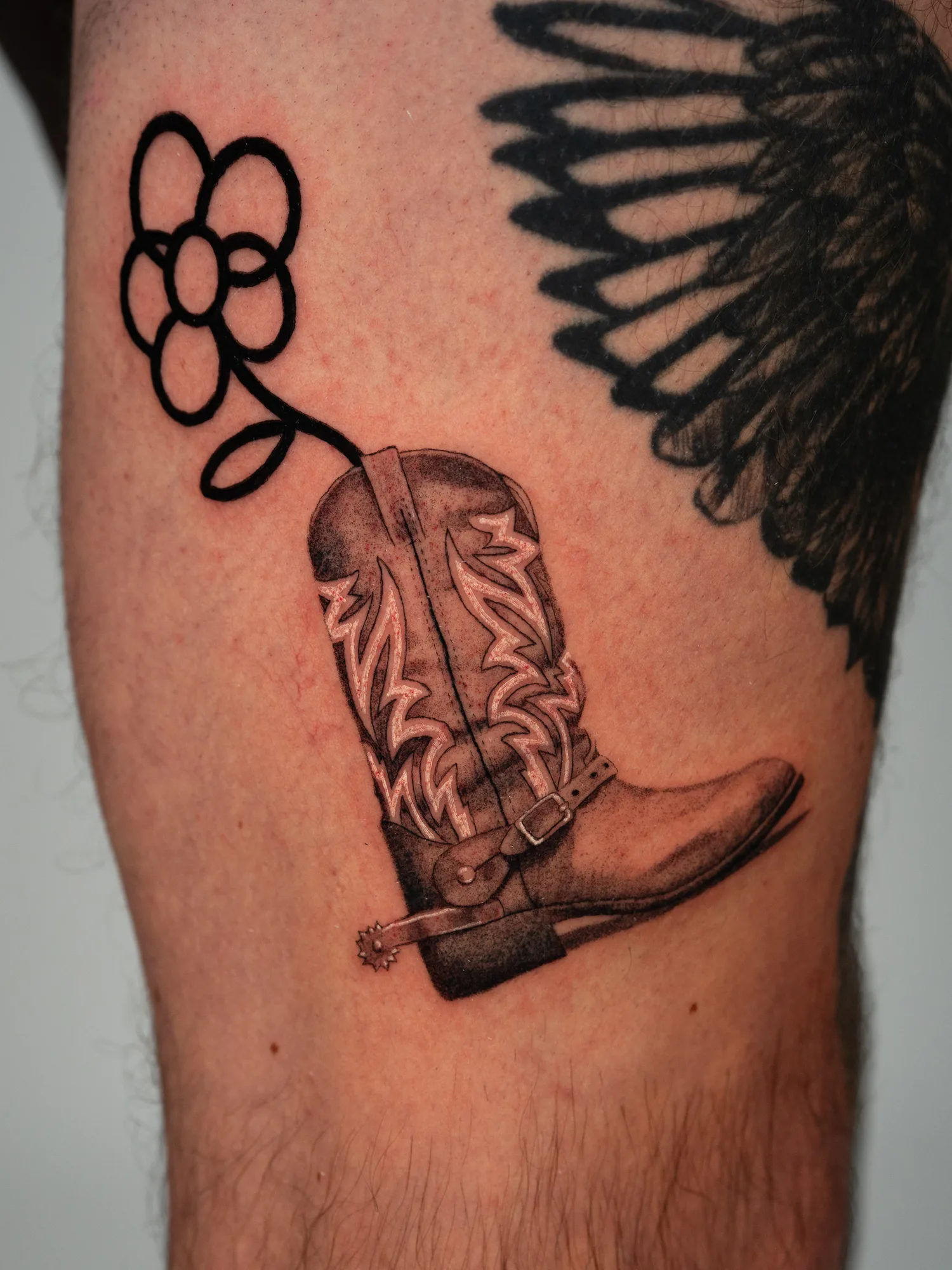 Tattoo of a micorealism cowboy boot with an illustrative stem coming out of the top.