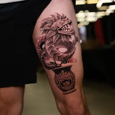 Tattoo depicting a feathered serpent hybrid and styled pottery on thigh.