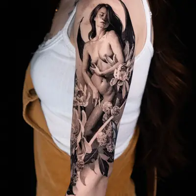 A detailed black and grey tattoo of a woman with wings and floral elements on an arm.