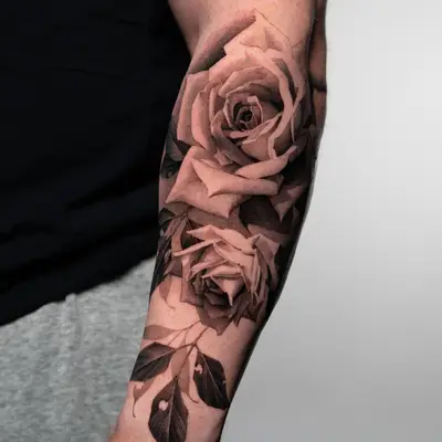 Black and grey tattoo of roses on the forearm, featuring detailed shading and leaves.