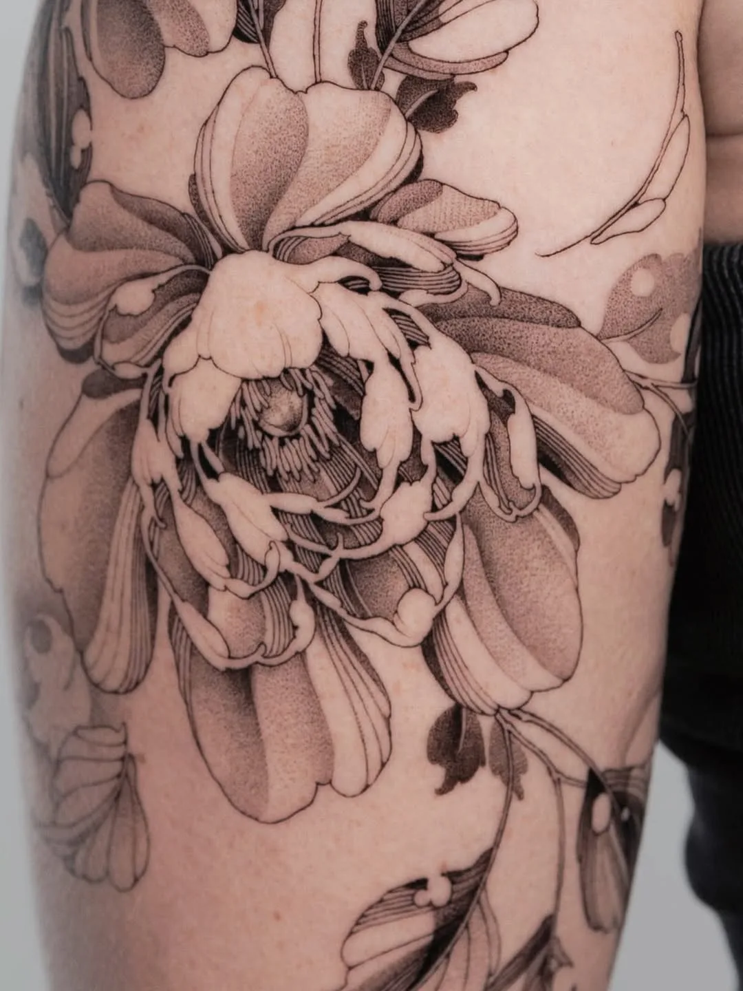 Fineline peony tattoo in black and grey on an outer forearm.