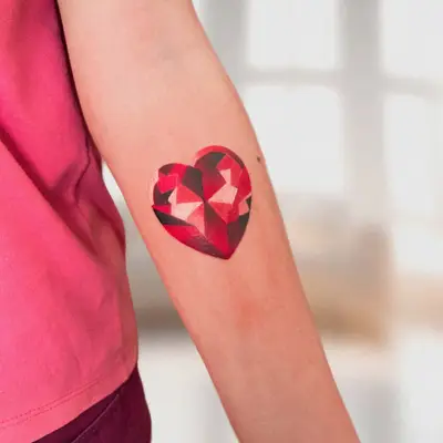 A vibrant red heart-shaped gemstone tattoo on the person's inner forearm.
