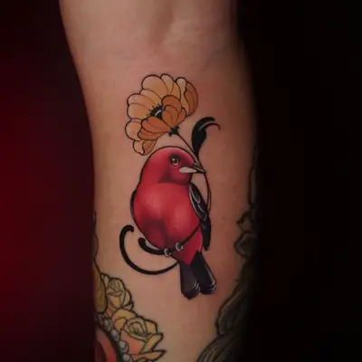 A vibrant red bird perched next to a yellow flower on a calf. tattoo.