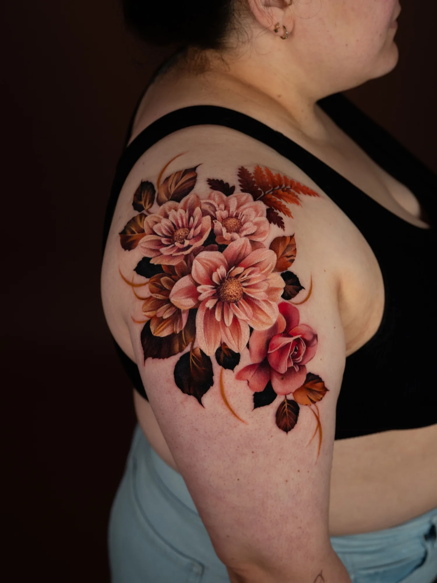 Colorful floral tattoo in a painterly realism style on an upper arm.