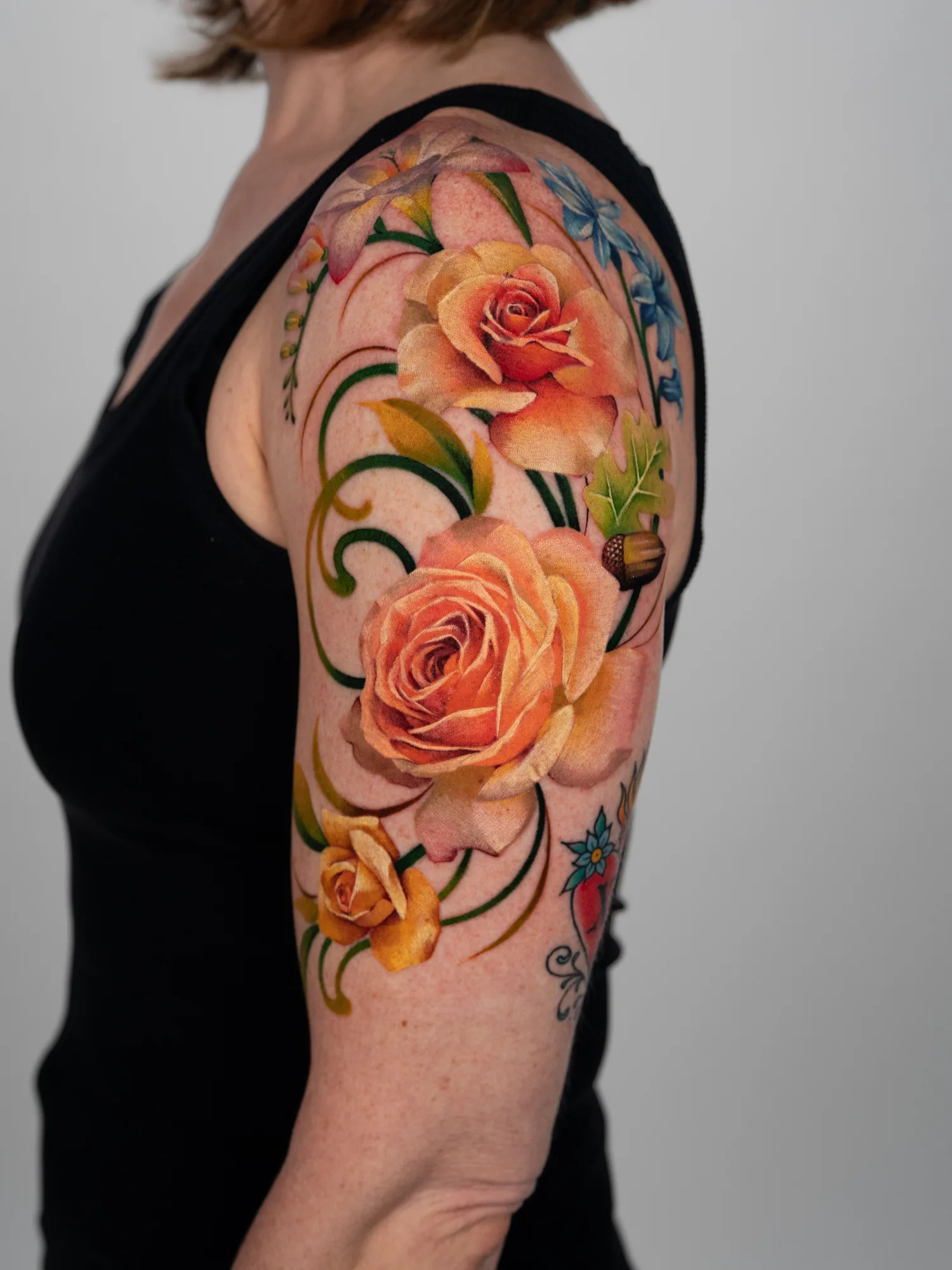 Colorful floral tattoo featuring roses and leaves on a woman's arm.