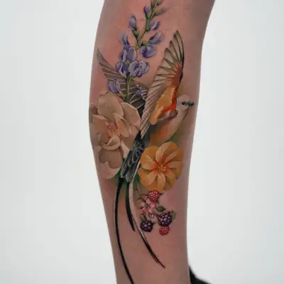 Color painterly tattoo on the side of the lower leg: a scissor-tailed flycatcher in flight with its long black tail feathers trailing down the calf, surrounded by purple wildflowers, a pale cream bloom, a yellow flower and blackberries.
