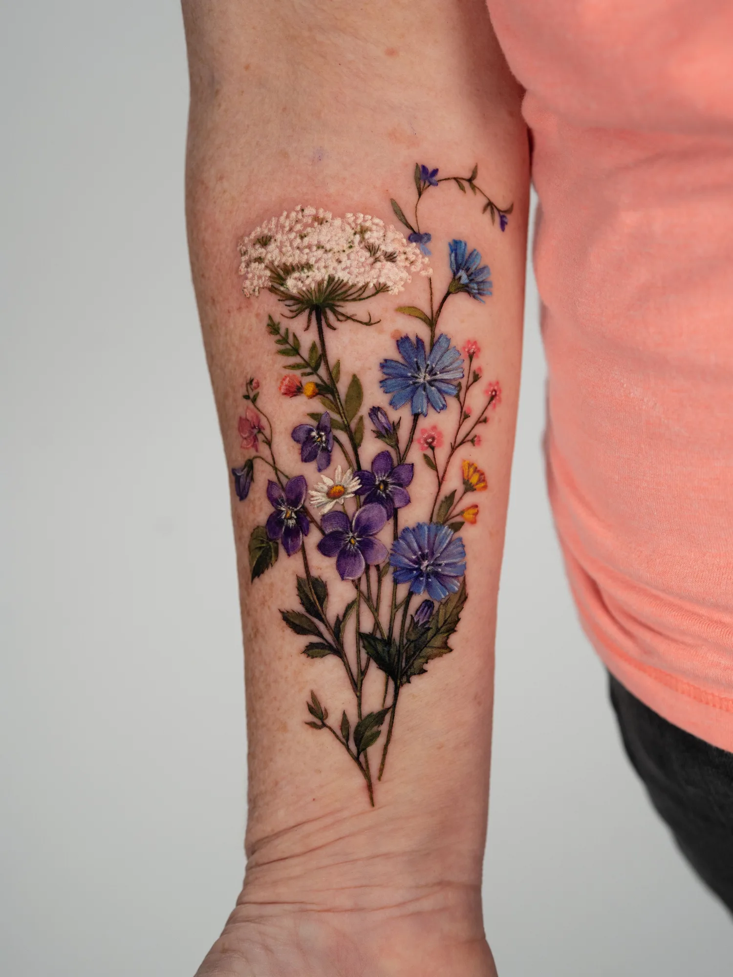 Colorful floral tattoo featuring various flowers on inner forearm.