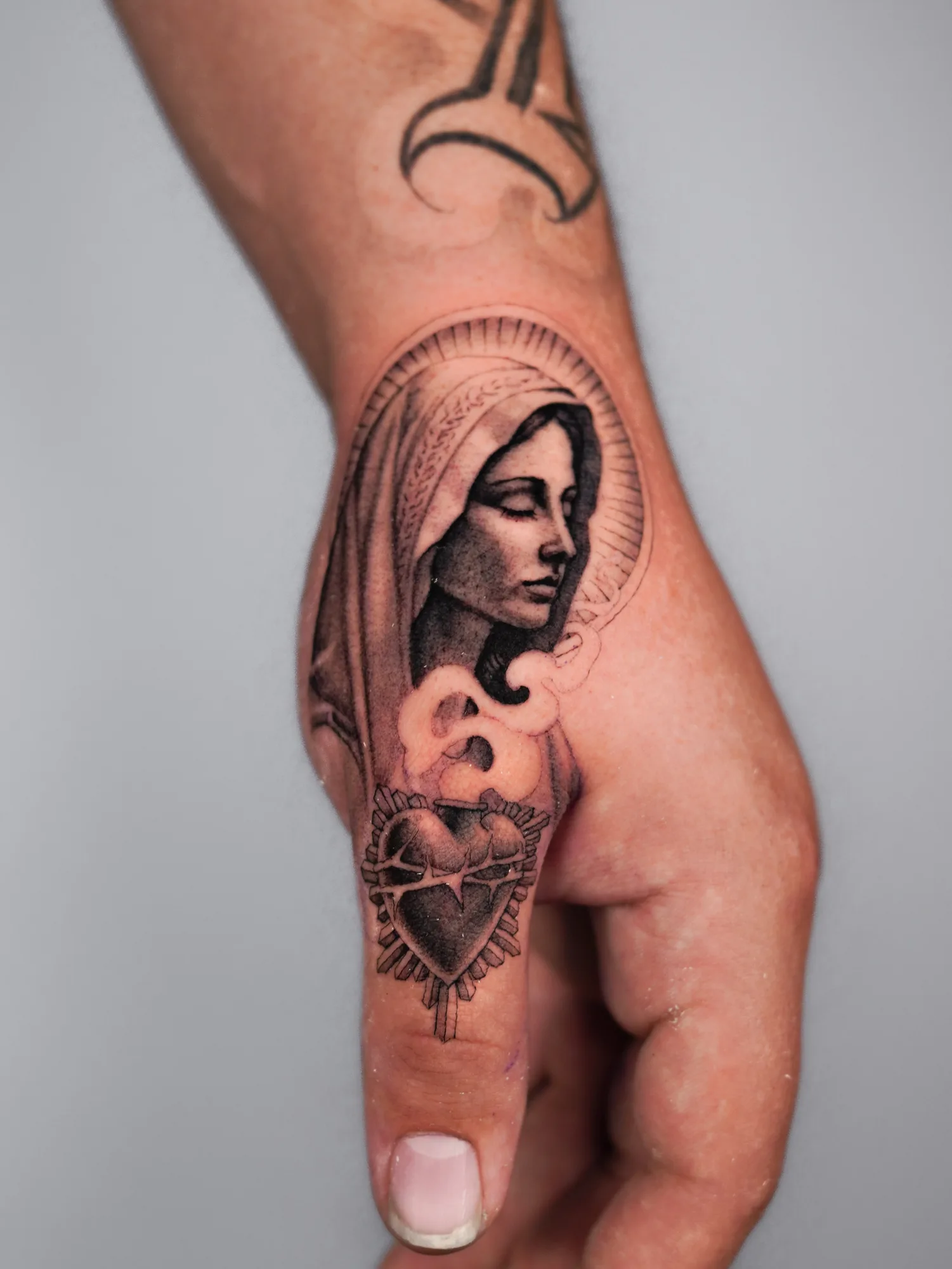 Tattoo of a religious figure and sacred heart on a hand.