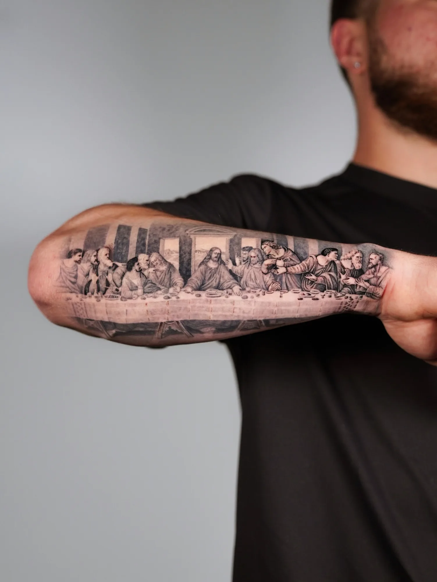 Black and grey tattoo of The Last Supper on forearm.