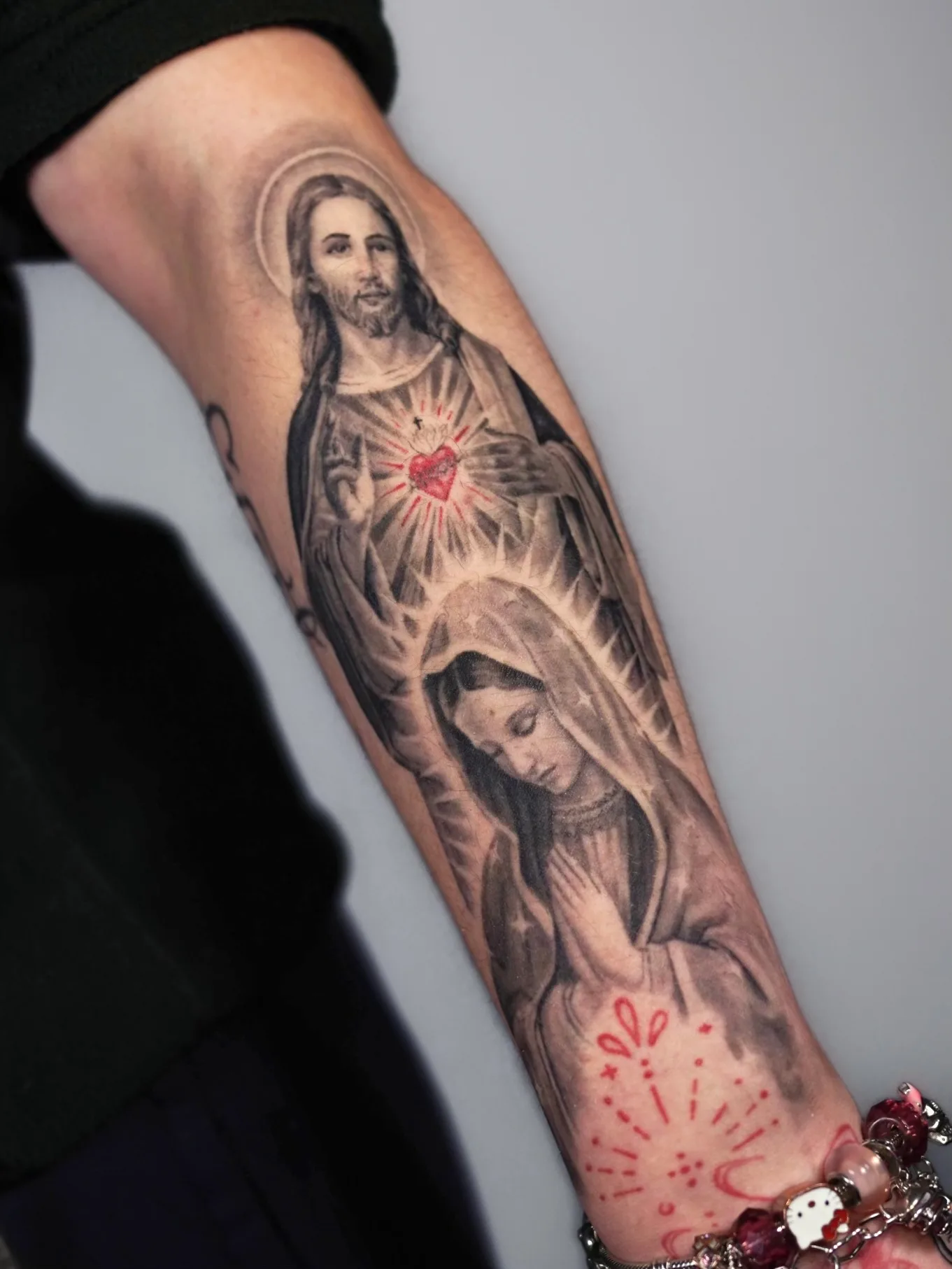 Tattoo of Jesus and Mary on forearm with red Sacred Heart detail.
