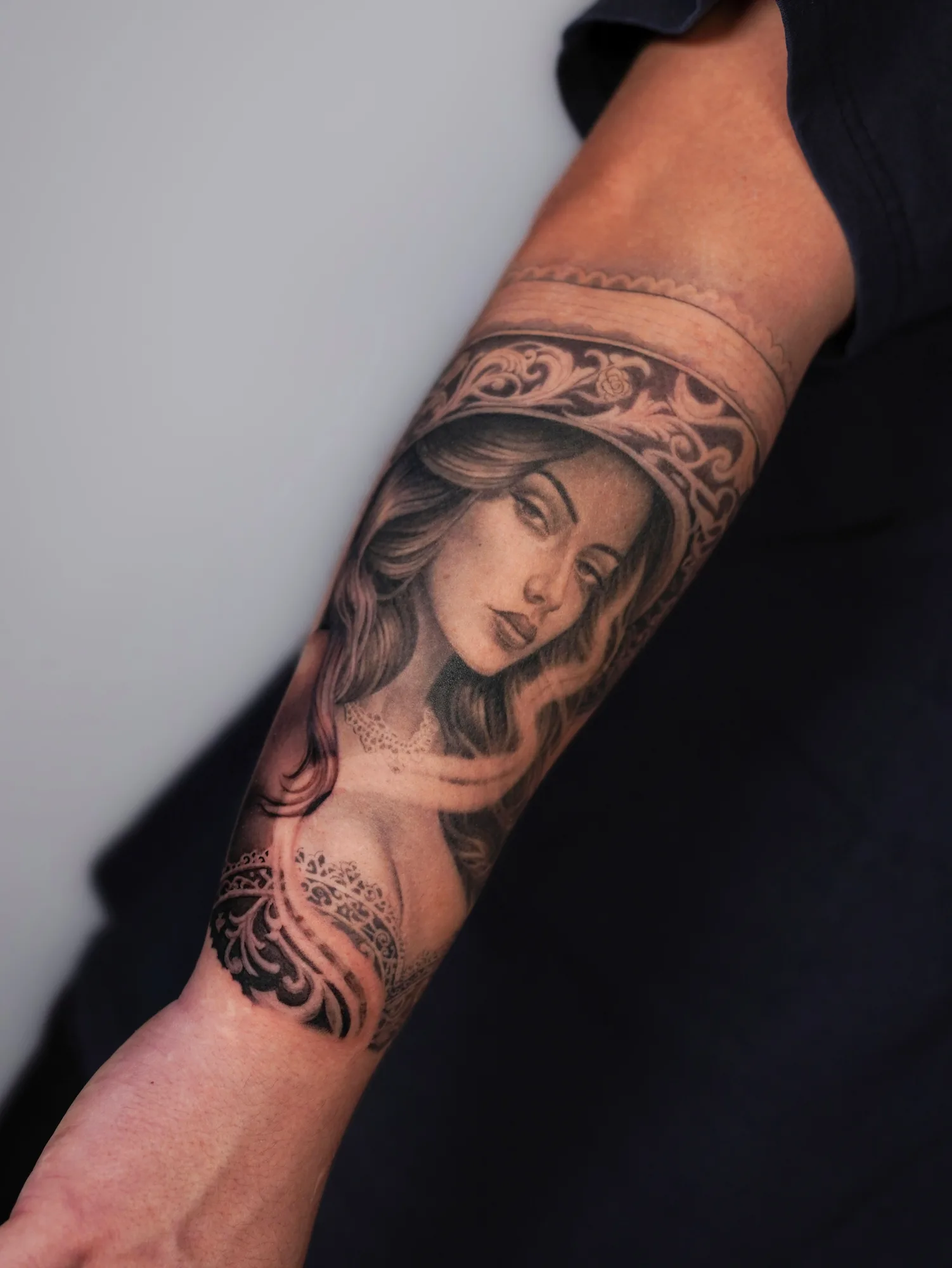 Tattoo of a woman's face with ornamental elements on a forearm.