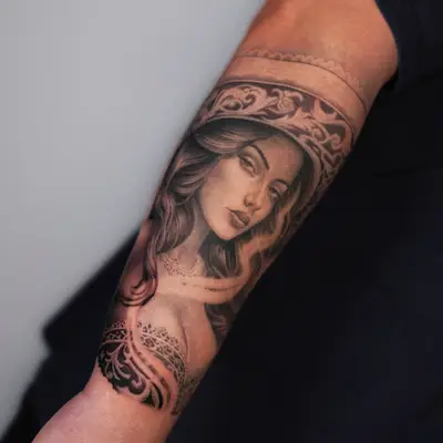 Tattoo of a woman's face with ornamental elements on a forearm.
