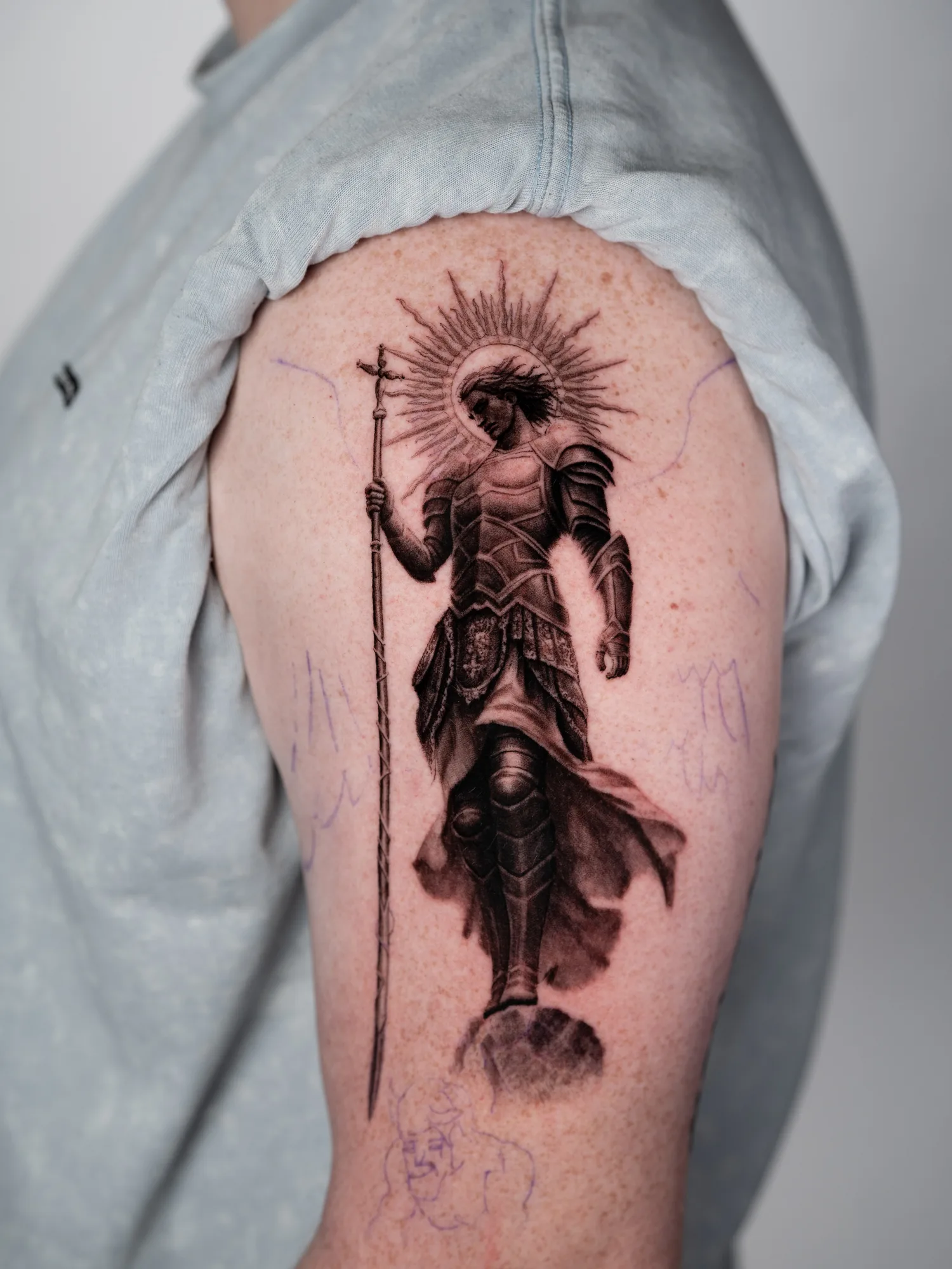Tattoo of armored figure with a halo and staff on upper arm.
