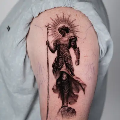 Tattoo of armored figure with a halo and staff on upper arm.
