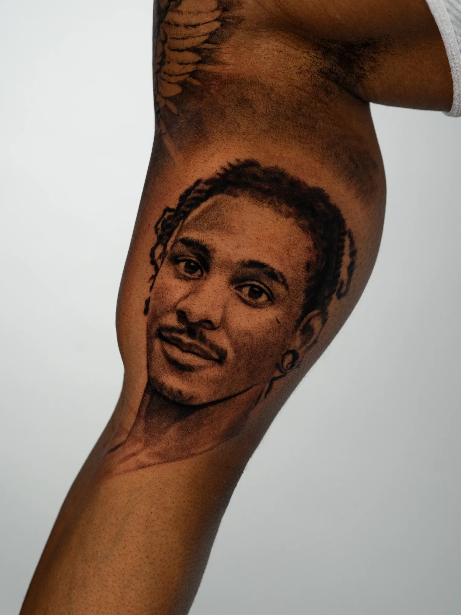 Realistic portrait tattoo of a young man on the inner arm.