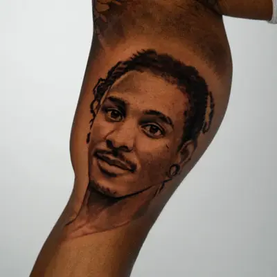 Realistic portrait tattoo of a young man on the inner arm.