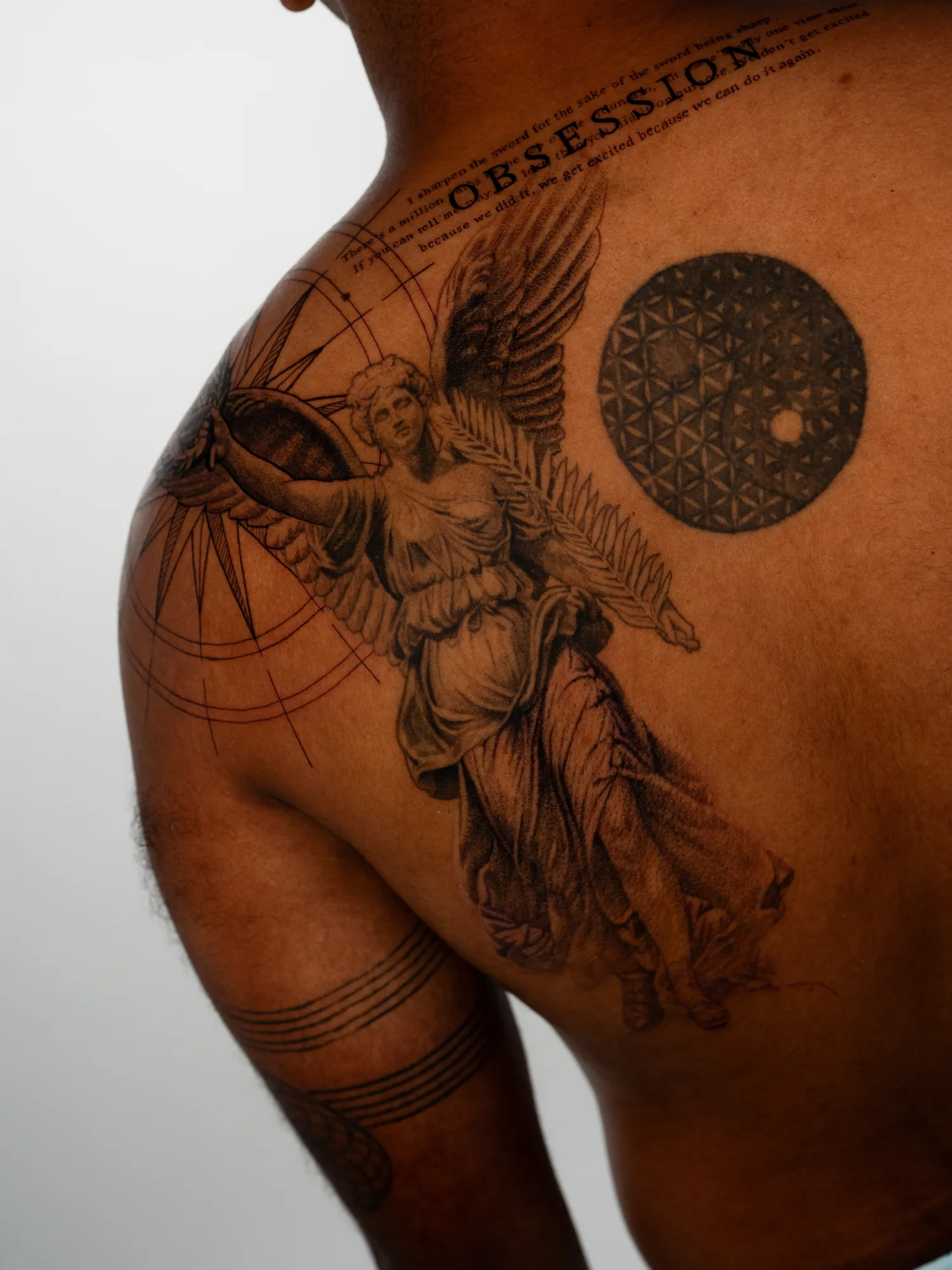 A back tattoo featuring a winged figure, geometric patterns, and text on a man's back.