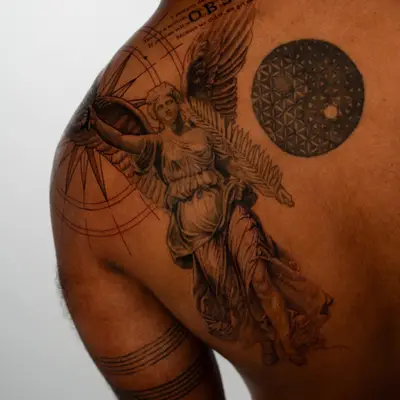 A back tattoo featuring a winged figure, geometric patterns, and text on a man's back.