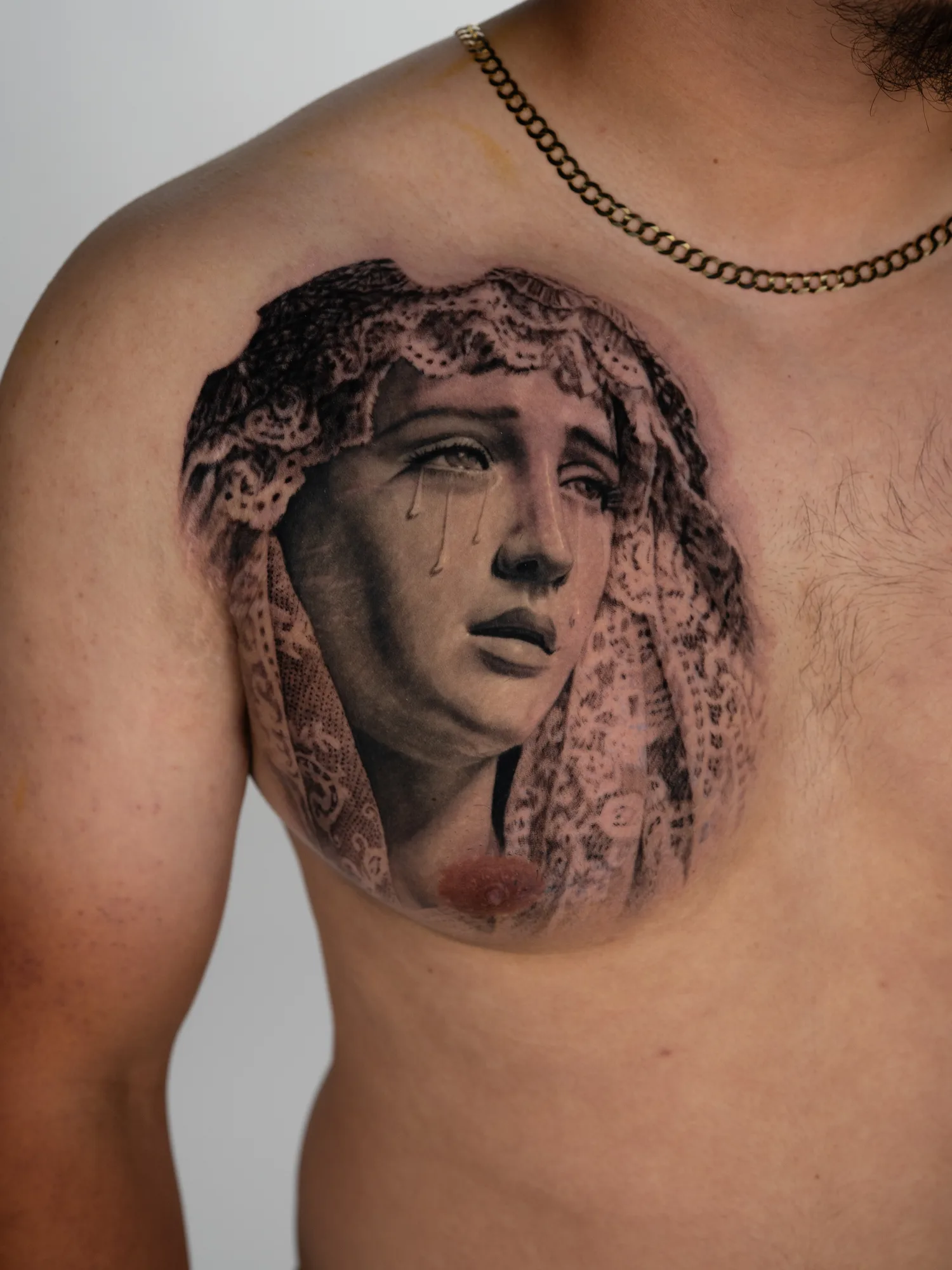 A realistic tattoo of a weeping Mary with a lace veil on a man's chest.