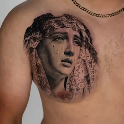 A realistic tattoo of a weeping Mary with a lace veil on a man's chest.