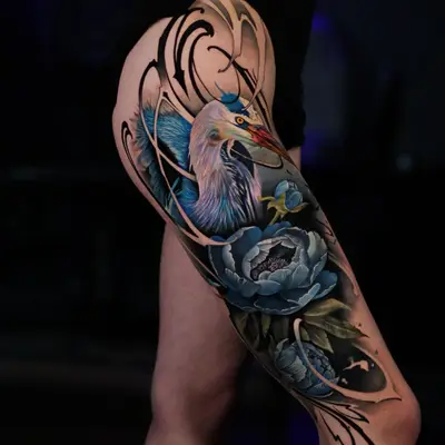 Colorful blue heron and floral tattoo on the thigh with calligraphy elements..