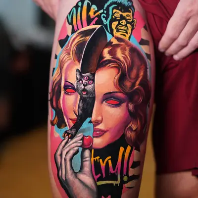 Colorful surreal tattoo with a woman's face, a cat, and graphic elements on a person's thigh.