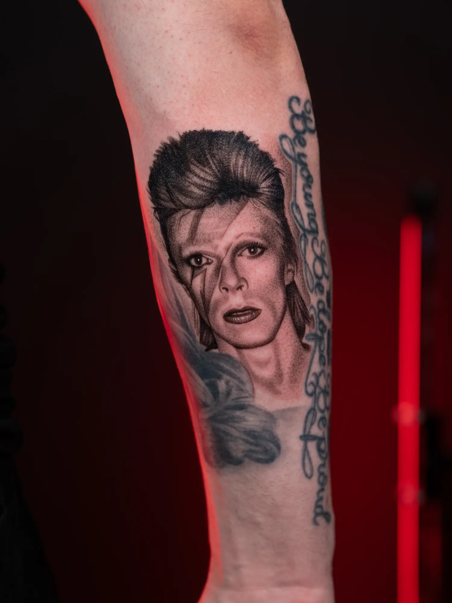 Forearm tattoo of a detailed portrait with lettering.