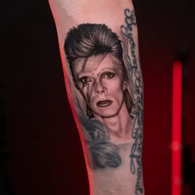 Forearm tattoo of a detailed portrait with lettering.