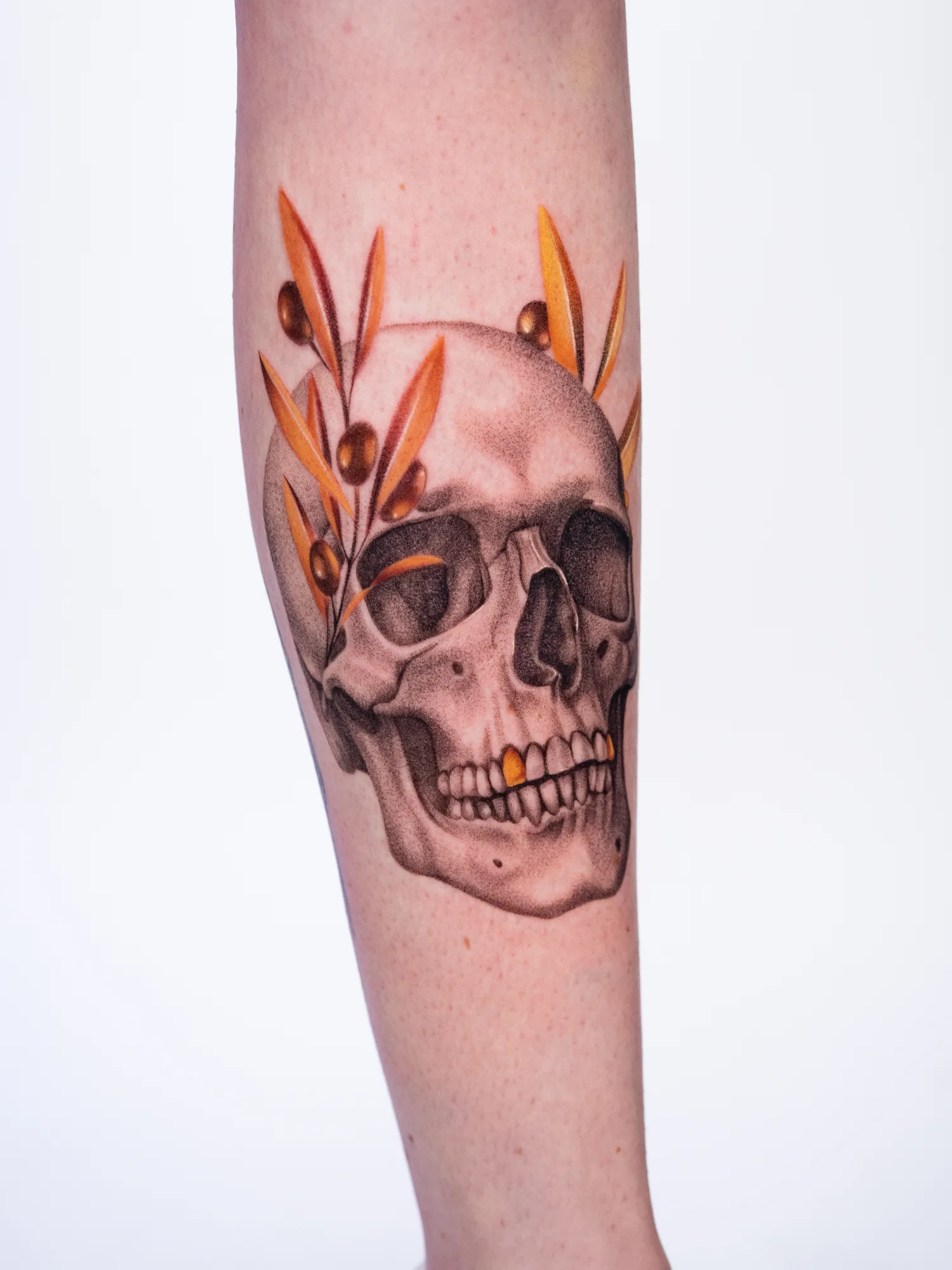 Skull tattoo with orange leaves on the forearm