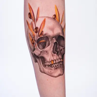 Skull tattoo with orange leaves on the forearm