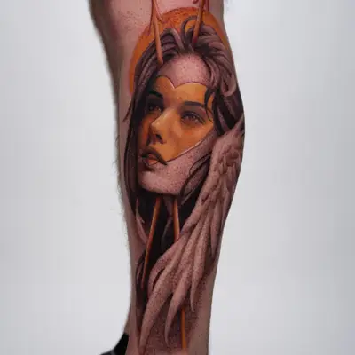 Tattoo of a woman's face with wings and a halo on a leg