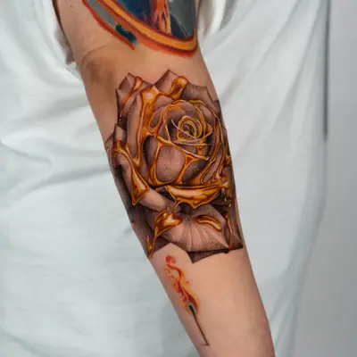 A realistic rose tattoo with a dripping gold effect on an outer forearm.