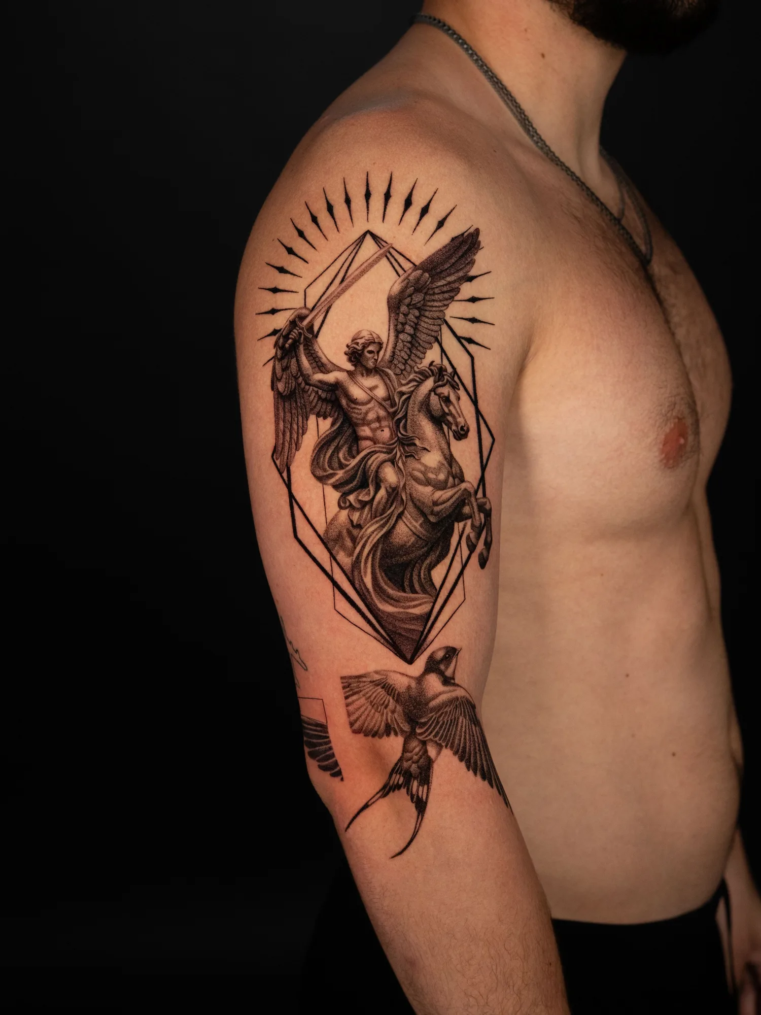 A detailed tattoo featuring a winged angel on a horse, with geometric elements and birds.