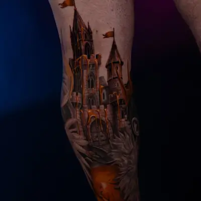 A detailed castle tattoo with gold accents on a leg.