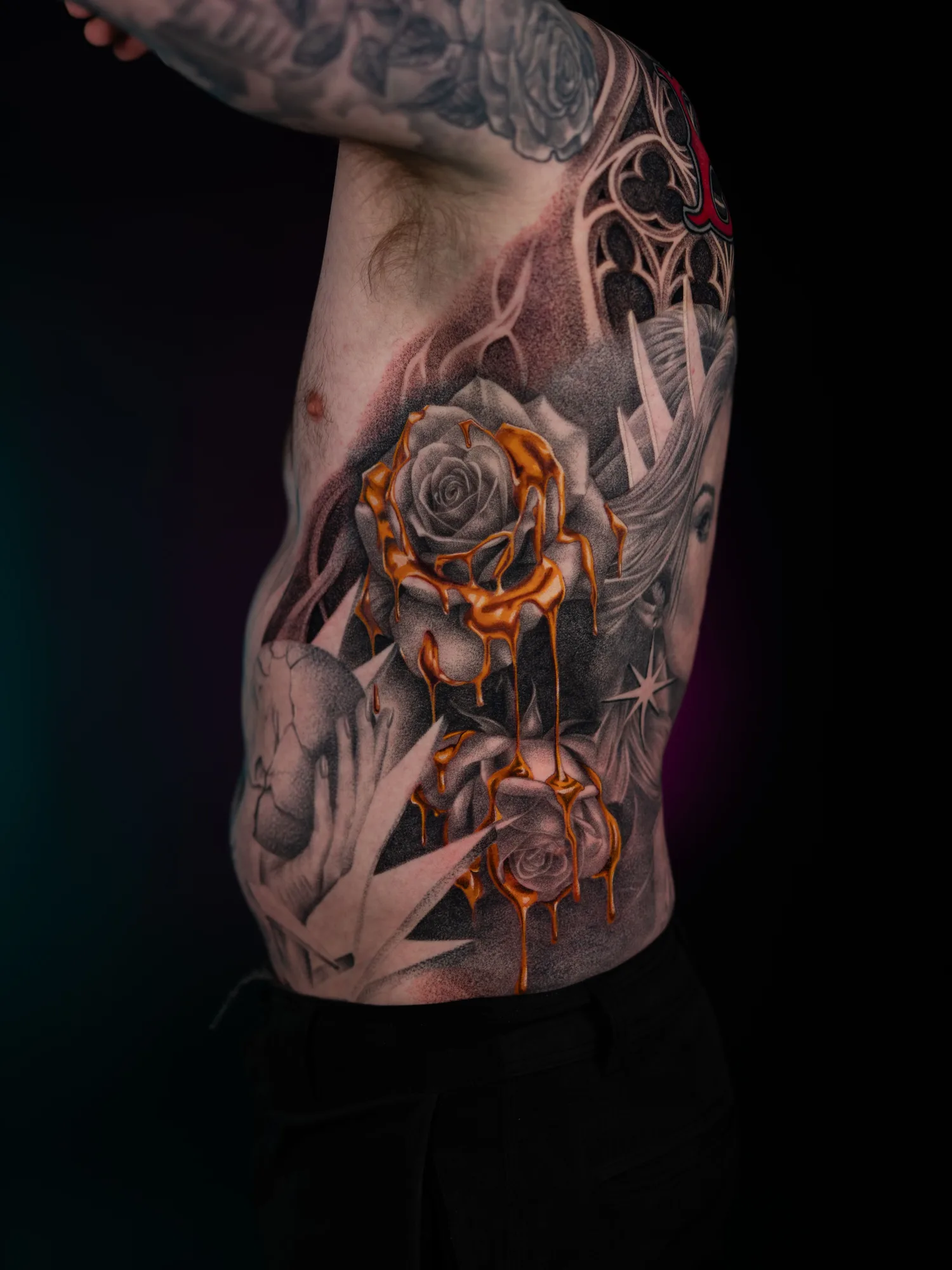 Tattoo of roses in black and grey on a rib cage with golden drips.