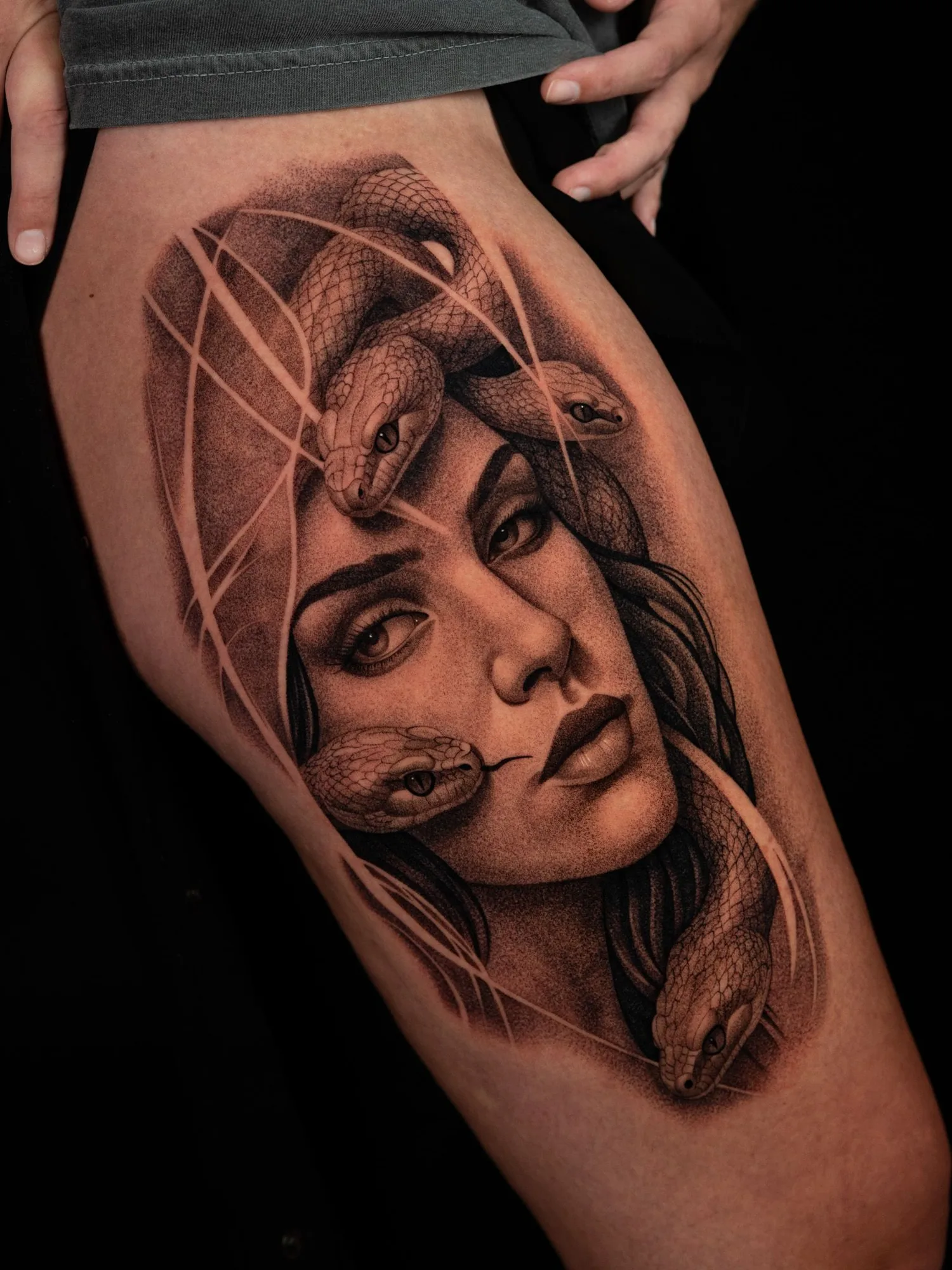 A black and grey realism portrait tattoo of medusa on the thigh. 