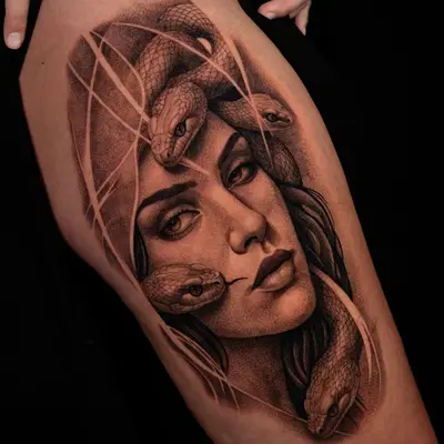 A black and grey realism portrait tattoo of medusa on the thigh. 