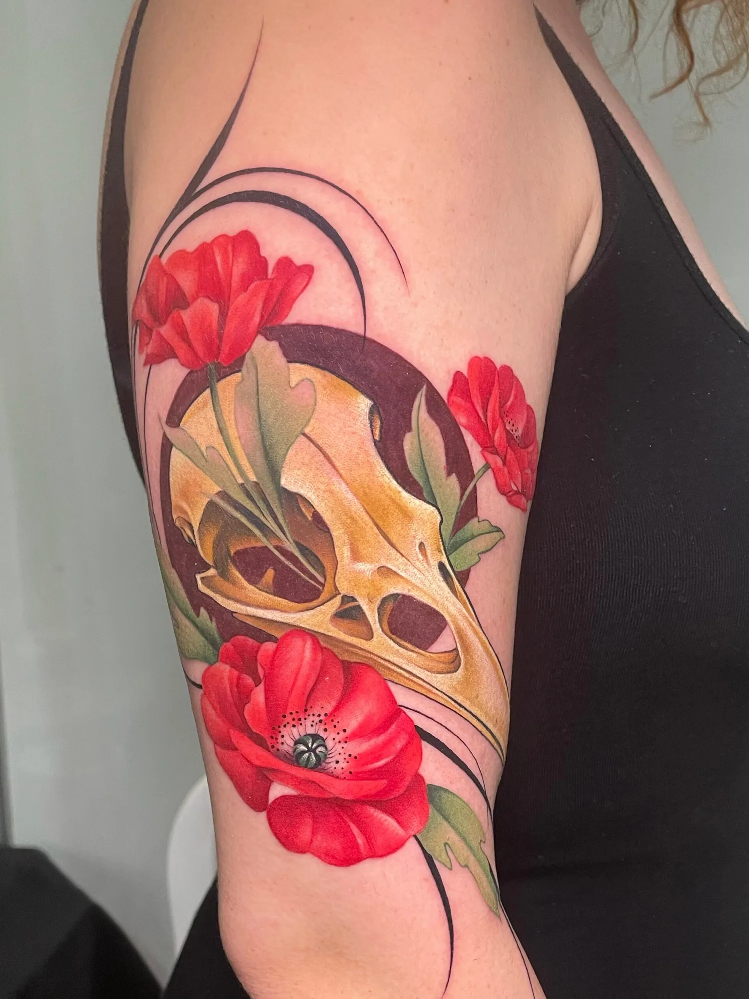 Tattoo of a skull with red poppies on upper arm.