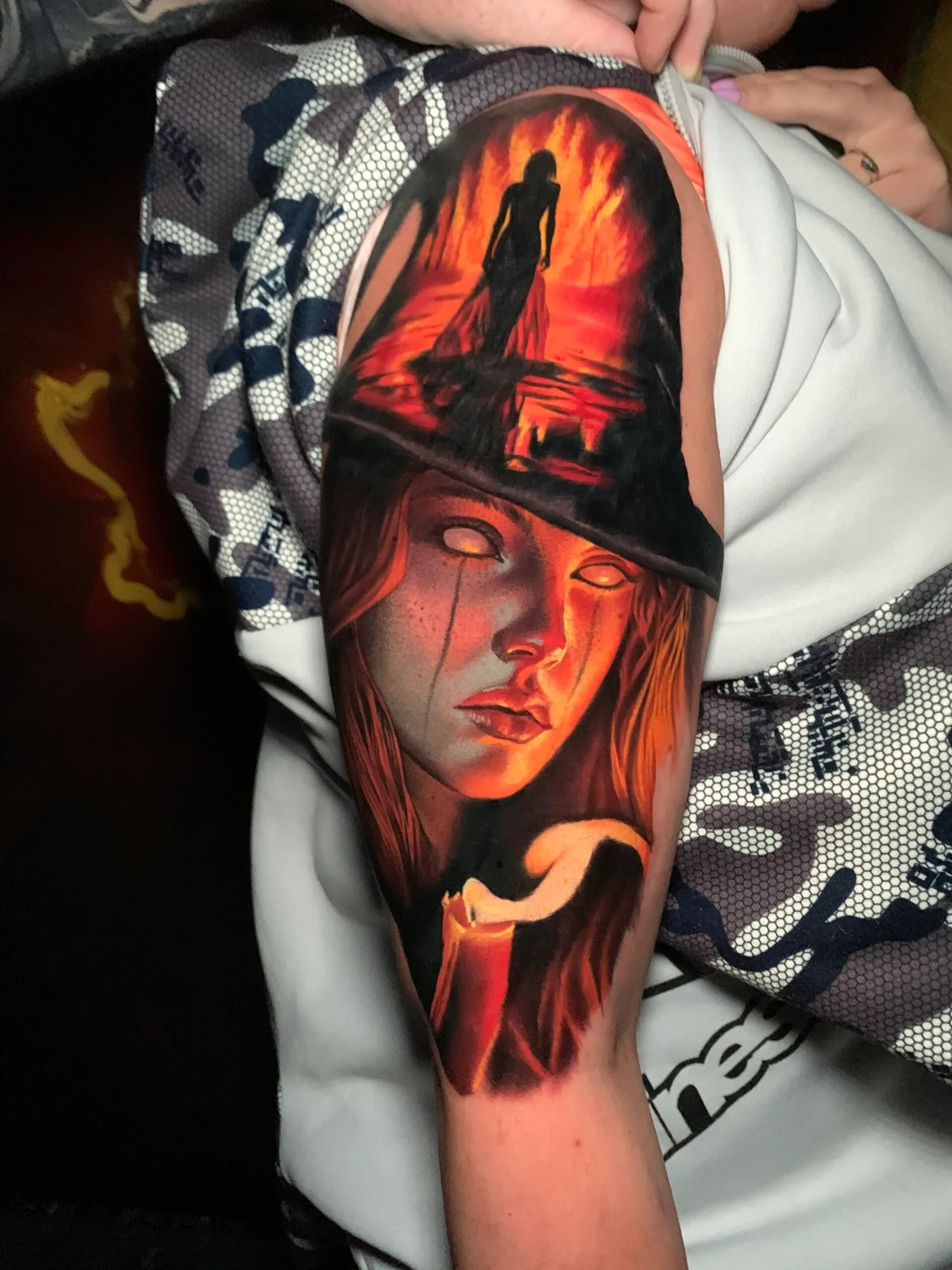 Tattoo of a witch and silhouette in flames on the upper arm.