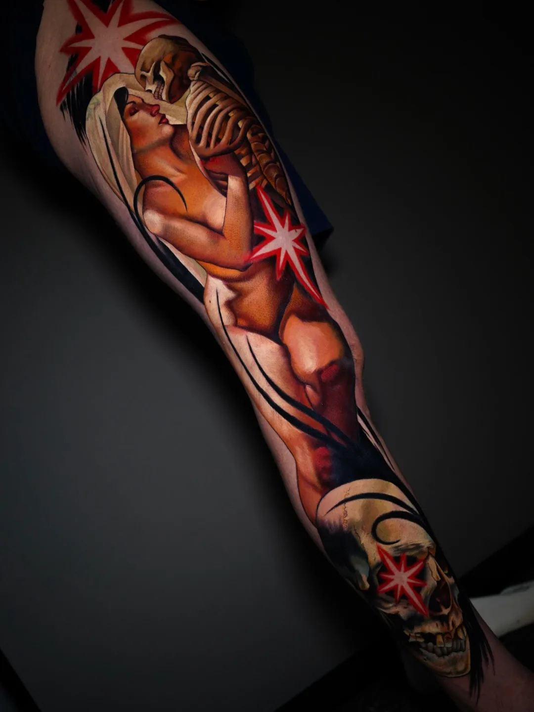 Tattoo featuring a woman embracing a skeleton with red starbursts.